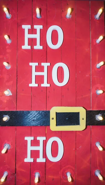 Noel Baba 'nın gülüşüyle kırmızı ahşap bir Noel posteri HO HO ve Noel Baba' nın tipik siyah kuşağı.
