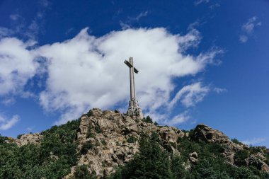 Madrid 'deki Düşenler Vadisi' nin tepesinde mavi gökyüzünde beyaz bulutlarla çapraz yap. Haç bir kayalık tepeye yerleştirildi.