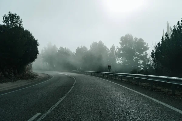 turning on a lonely road in a foggy mountain sunrise with a kilometer sign in the side road. Road surrounded by a forest