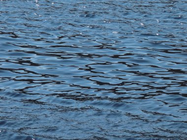 Koyu mavi deniz yüzeyi, küçük dalgalar ve güneş yansıması..