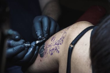 Kadının koluna COVID 'den korunan bir makine dövmesi yapılmış. Yaşam tarzı. Siyah lateks eldiven giyen bir dövmeci. Dövme bir kadın yüzü..