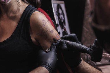 Kadının koluna COVID 'den korunan bir makine dövmesi yapılmış. Yaşam tarzı. Siyah lateks eldiven giyen bir dövmeci. Dövme bir kadın yüzü. Taslak arka planda.