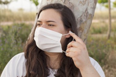 Bayan Covid-19 'dan korunmak için açık havada bir maske tarafından korunuyor. Doğal kaynaklar, ağaçlar ve temiz hava..