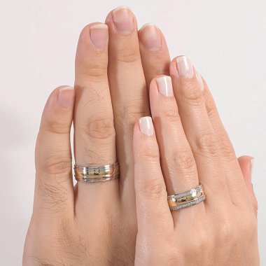 Erkek ve kadın modelin parmağına takılmış bir çift gümüş alyans..