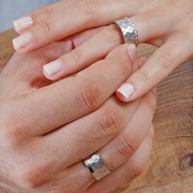 Erkek ve kadın modelin parmağına takılmış bir çift gümüş alyans..