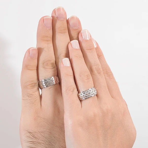 A pair of silver wedding rings worn on the finger of the male and female model.