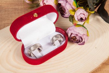 Ahşap zeminde zarif çiçeklerle süslenmiş kırmızı kadife bir kutuda alyanslar..