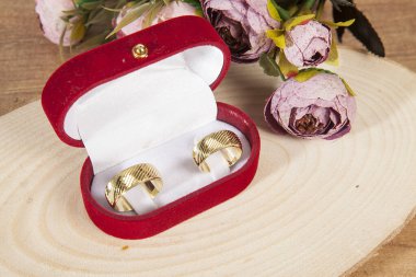 Ahşap zeminde zarif çiçeklerle süslenmiş kırmızı kadife bir kutuda alyanslar..