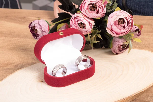 Wedding rings in a red velvet box decorated with elegant flowers on wooden floor.