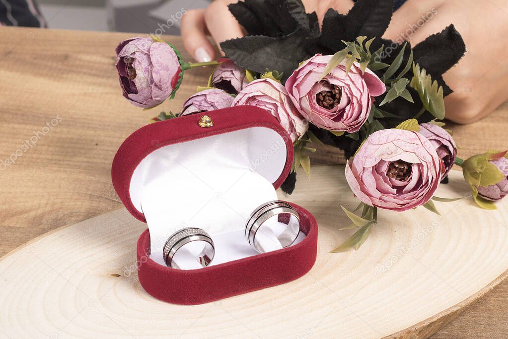Wedding rings in a red velvet box decorated with elegant flowers on wooden floor.