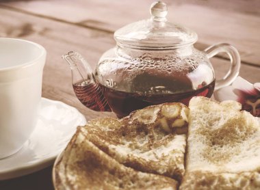 Yığın krep ve ahşap bir masa üzerinde beyaz bir kupa ile plaka