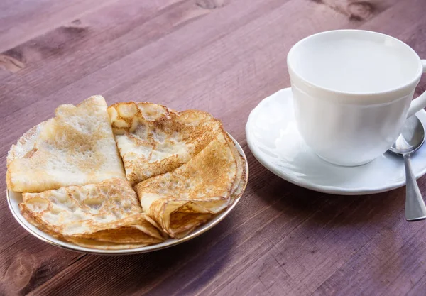 Yığın krep ve ahşap bir masa üzerinde beyaz bir kupa ile plaka