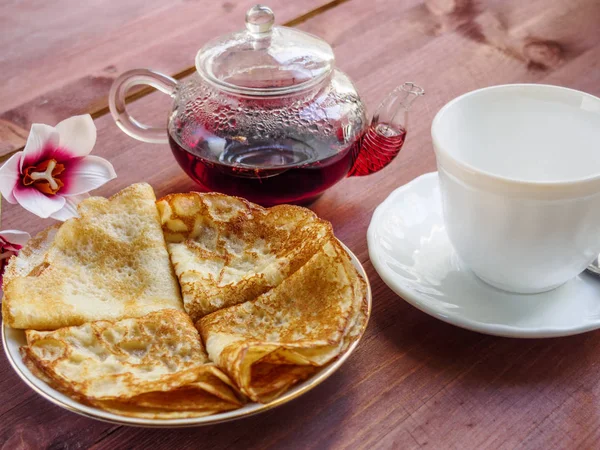 Bir tabak krep ve beyaz bir bardak ve bir demlik çay üzerinde ahşap bir masa ile