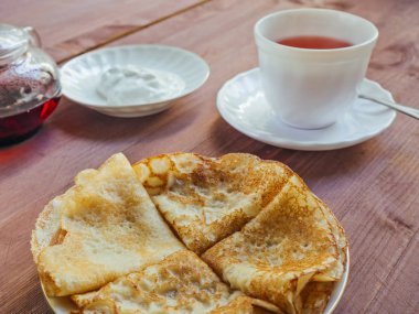 Bir tabak krep ve beyaz bir bardak ve bir demlik çay üzerinde ahşap bir masa ile