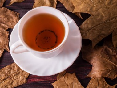 Sonbahar yaprakları ile çevrili bir ahşap zemin üzerine yeşil çay bardağı