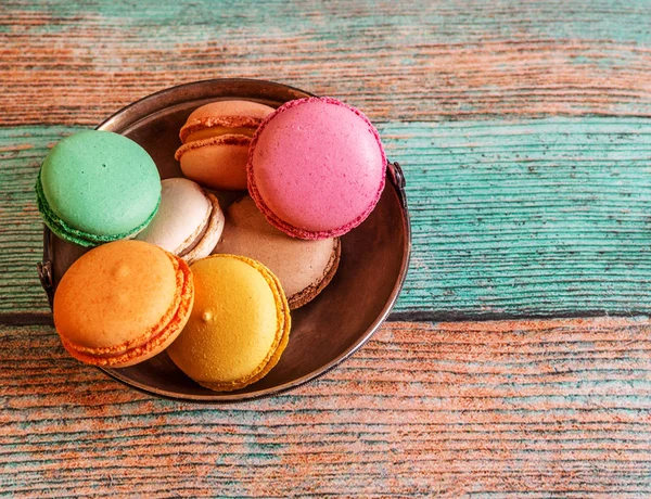 Tahta bir masanın üzerinde Fransız badem kurabiyesi olan metal bir tabak.