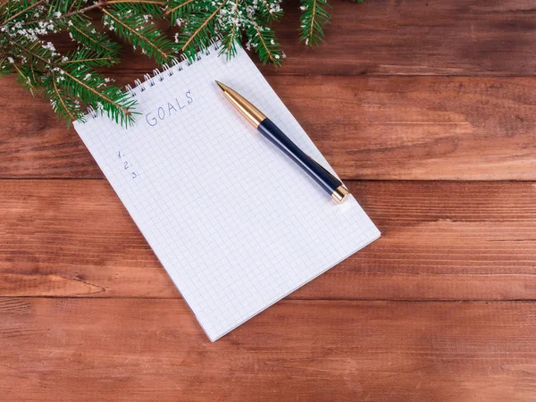 Notepad for writing resolution and goals for the New Year, spruce branches on a wooden background with copy space
