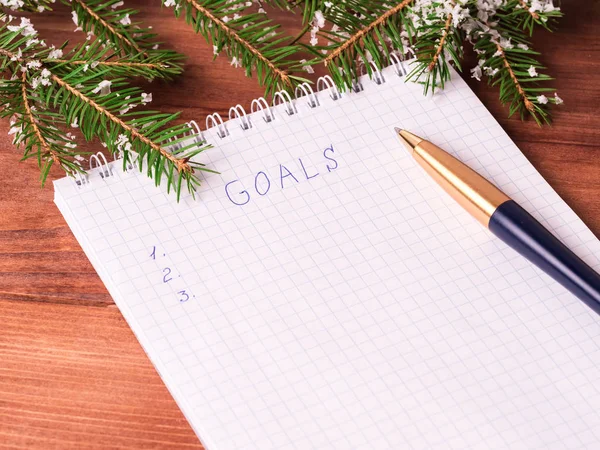 Notepad for writing resolution and goals for the New Year, spruce branches on a wooden background with copy space