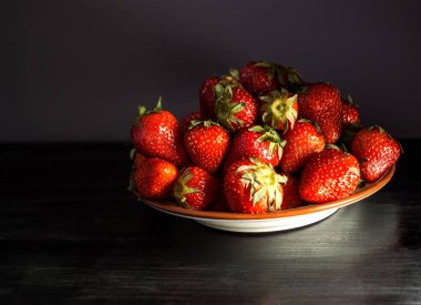 Karanlık bir arka plan üzerinde toplanan taze çilek ile plaka