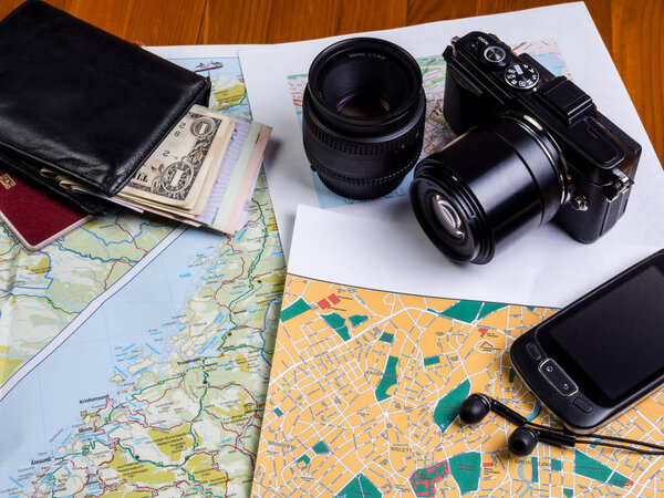 Maps on the table, a black camera with lenses and a smartphone with headphones