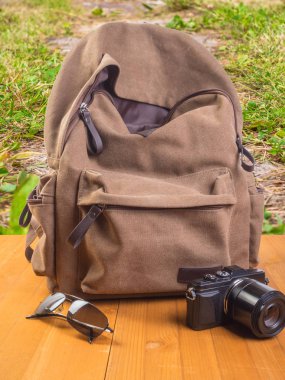 Tahta bir arka planda sırt çantası, kamera ve gözlük.