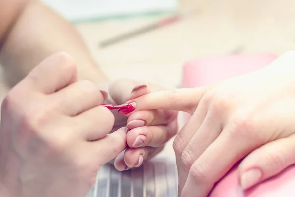 Manicurist paints nails with red lacquer in the salon.