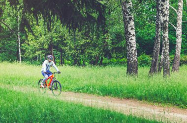 Bir kask bir bisikletçi ormanın içinden bir bisiklet yolu rides..