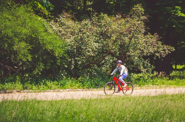 Cyclist in helmet on orange bike riding in park.