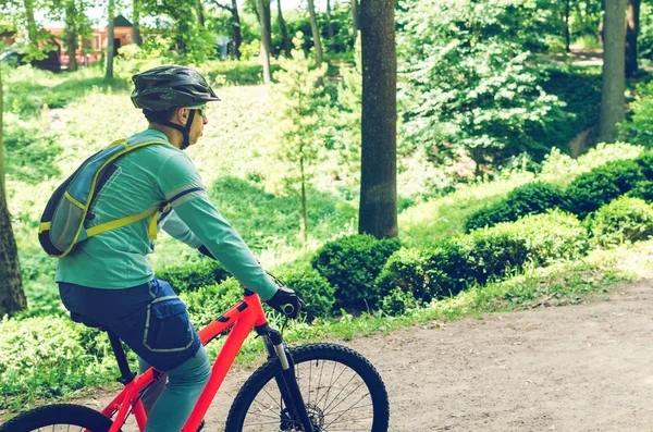 Cyclist in helmet on orange bike riding in park.