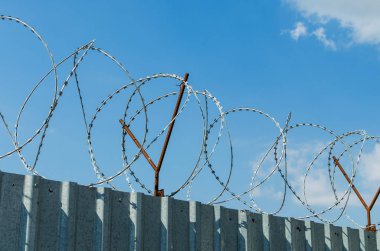 Mavi gökyüzü arka plan üzerinde dikenli tel ile metal çit.