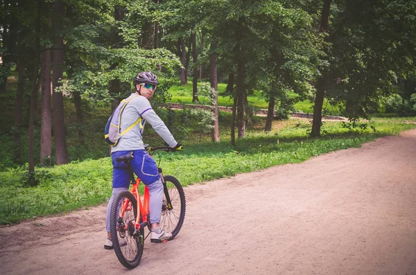 Cyclist in helmet on orange bike riding in park.