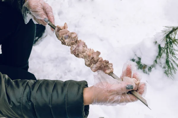 stock image Women's hands strung meat on a skewer in the winter forest.