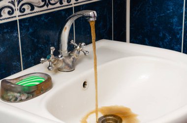 Beyaz bir lavabo kirli paslı su akar.