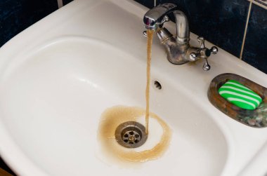 Beyaz bir lavabo kirli paslı su akar.