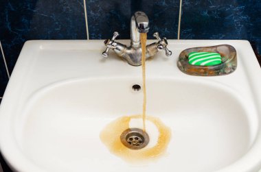 Beyaz bir lavabo kirli paslı su akar.