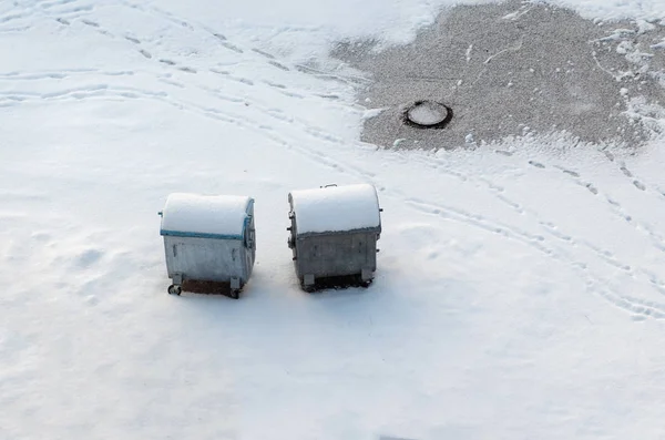Metal old garbage cans are standing in the yard in the snow in winter.