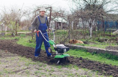 Bahar bahçede tiller makine ile çalışan adam.