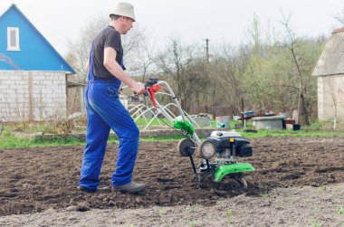 Bahar bahçede tiller makine ile çalışan adam.