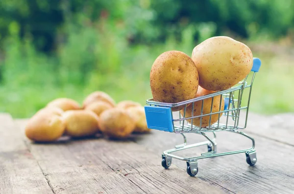 Un pequeño carrito de compras con patatas en una vieja mesa de madera — Foto de Stock