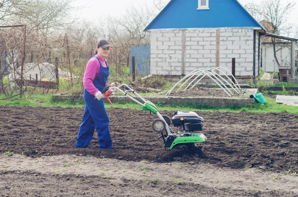 Chica joven que trabaja en un jardín de primavera con un cultivador —  Fotos de Stock