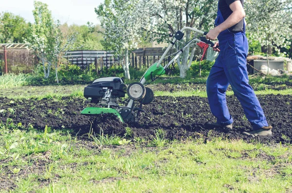 Uomo che lavora nel giardino primaverile con macchina fresatrice — Foto Stock