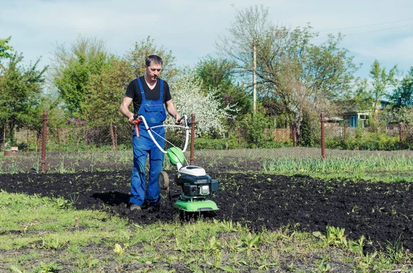 Uomo che lavora nel giardino primaverile con macchina fresatrice — Foto Stock