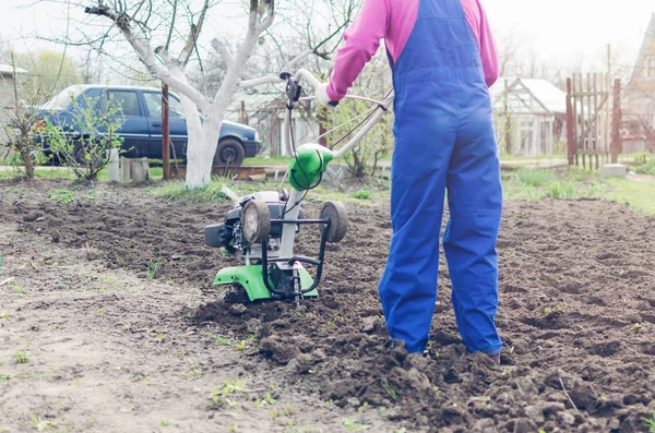 Jovem trabalhando em um jardim de primavera com um cultivador — Fotografia de Stock