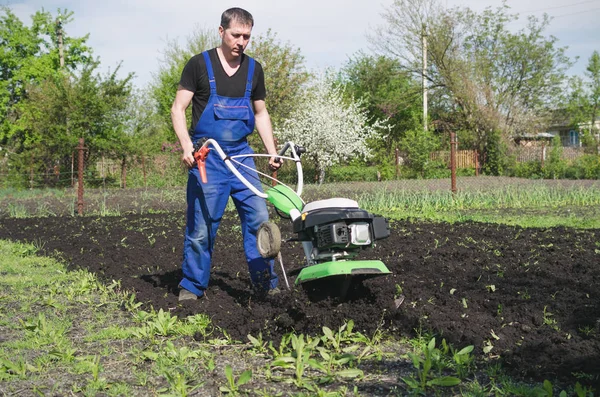 Uomo che lavora nel giardino primaverile con macchina fresatrice — Foto Stock