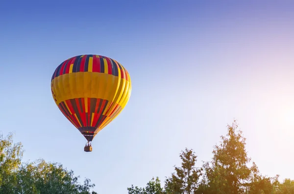 Montgolfière colorée vole dans le ciel bleu au-dessus des arbres — Photo