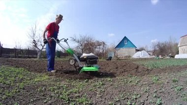 Adam bahçedeki toprağı bir dümenciyle işliyor, toprağı ekime hazırlıyor.