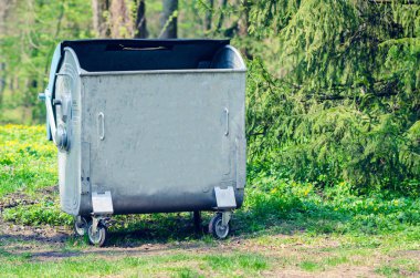 Ağaçlar arasında halka açık bir parkta metal çöp tenekesi