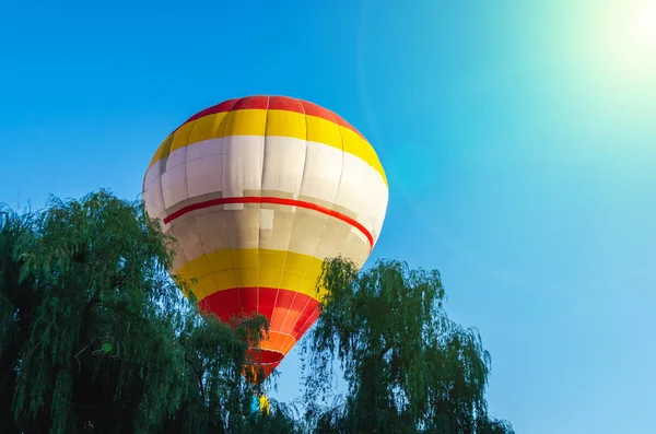 Balão de ar quente colorido está voando no céu azul acima das árvores — Fotografia de Stock