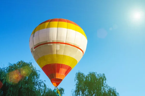 Renkli sıcak hava balonu ağaçların yukarıda mavi gökyüzünde uçuyor — Stok fotoğraf