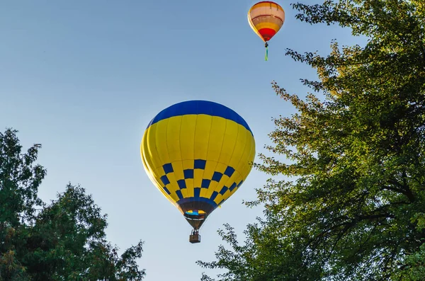 Montgolfière colorée vole dans le ciel bleu au-dessus des arbres — Photo